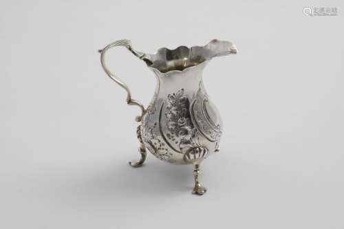 A GEORGE II SMALL BALUSTER CREAM JUG on three legs with a sh...