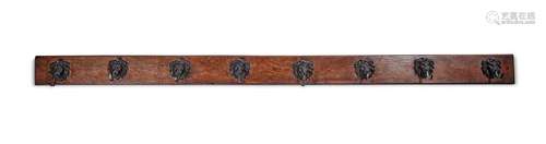 A long oak wall mounted coat rack with eight bronze lion mas...