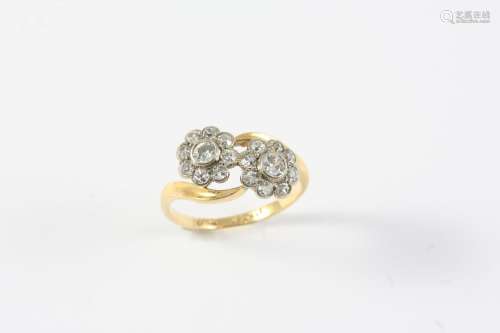 A DIAMOND CROSS-OVER RING set with two flowerheads each moun...