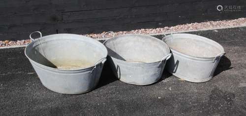 Three graduated galvanised tubs, each of oval form, applied ...