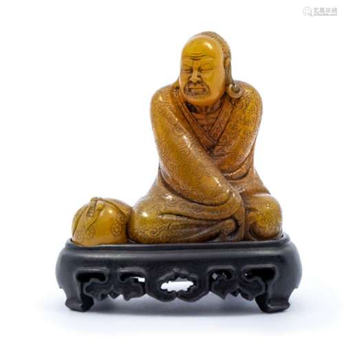 A soapstone carved figure of a luohan, the figure clad in fl...