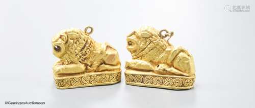 A pair of Etruscan style yellow metal recumbent lion pendant...