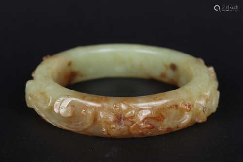 A CARVED GREENISH AND BROWNISH JADE BANGLE