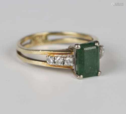 A gold ring, claw set with a rectangular cut emerald between...