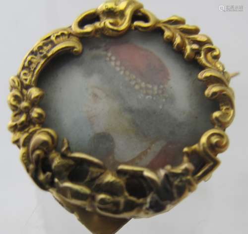 A yellow metal miniature brooch of a lady in a red hat, poss...