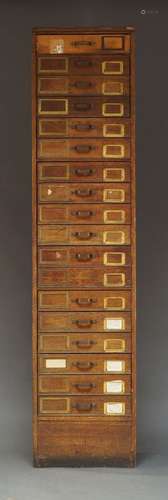 A narrow oak filing cabinet, with eighteen drawers on a plin...