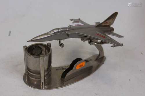 A desk stand, surmounted by a fighter jet with clock and pen...