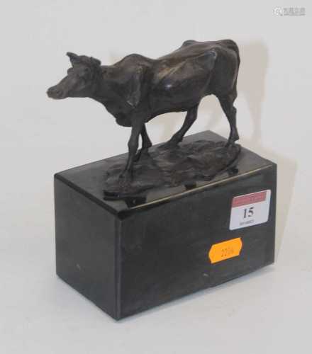 A modern bronzed metal model of a cow raised on a black faux...
