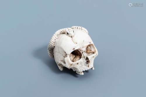 A Japanese ivory okimono of a human skull entwined with a sn...