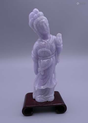 A lavender jade carving of Guanyin, on a small wooden stand....