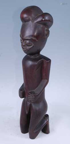 A wooden ancestor figure, carved in kneeling pose with arms ...