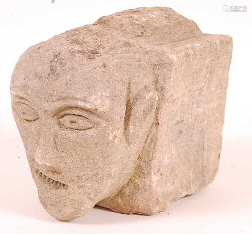 * A limestone block, carved as a male head with arched brows...