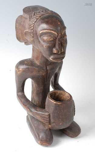 * A carved wooden figure in kneeling pose with offerings bow...