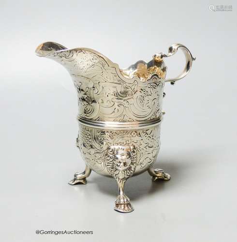 An engraved white metal helmet shaped cream jug, on tripod f...