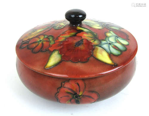 A Moorcroft pot decorated in an orchid pattern on a red grou...