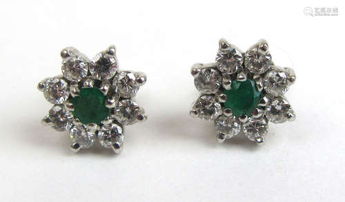 A pair of white metal, emerald and diamond cluster earrings....