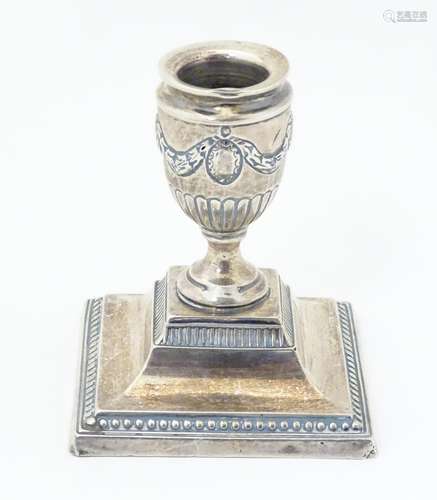 A silver candlestick of urn form on a squared base,