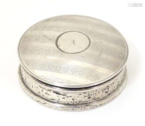 A silver pill box of circular form with banded engine