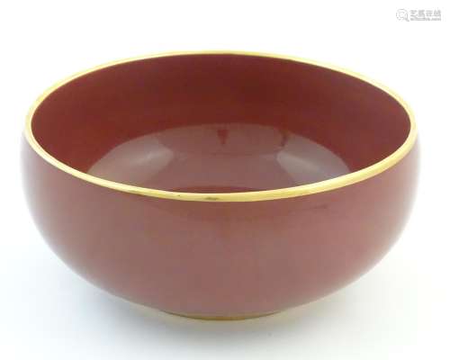 A Japanese bowl with a red glaze and gilt rim.