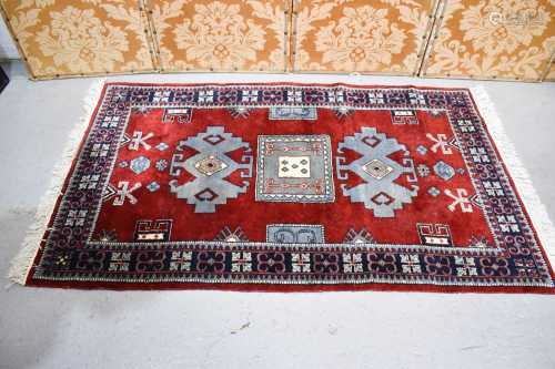 A Middle Eastern rug with a red ground, blue stylised motifs...