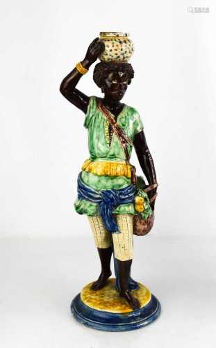 A 19th century majolica figure of an African boy holding a b...