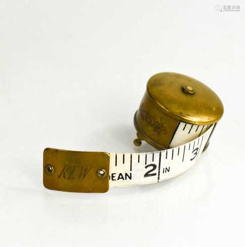 A vintage brass tape measure with engraved initials R.E.W.
