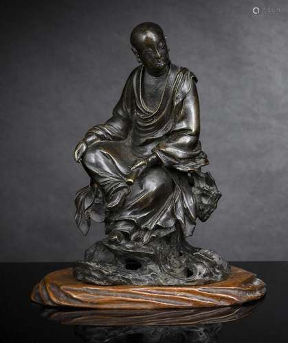 A BRONZE FIGURE OF A SEATED LUOHAN ON A ROCK WITH WOOD STAND