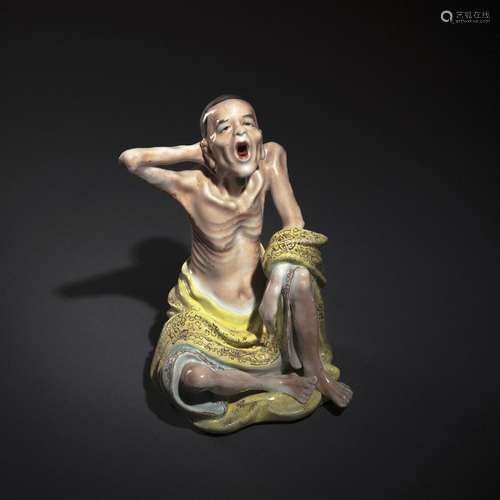 A POLYCHROME DECORATED PORCELAIN FIGURE OF A SEATED YAWNING ...