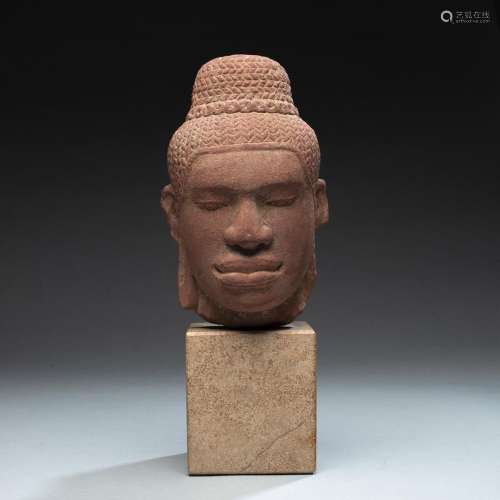A RED SANDSTONE HEAD OF A MALE DEITY MOUNTED ON A STAND