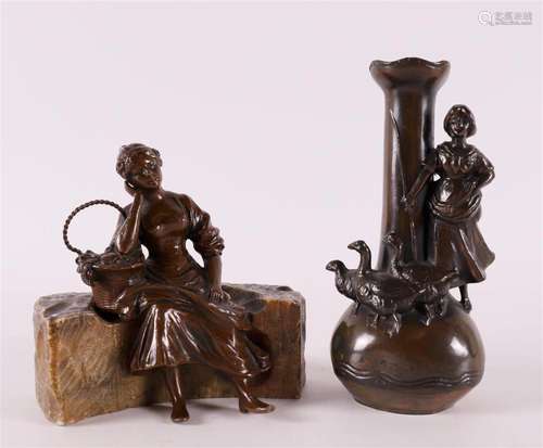 A brown patinated white metal seated woman with a flower bas...