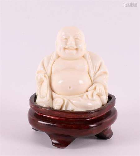 An ivory laughing Buddha on a wooden pedestal, ca. 1920.