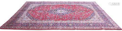 A PERSIAN KASHAN CARPET, the bright red field with dark blue...