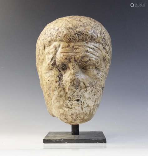 A worn marble male head carved with deeply furrowed brow, wi...