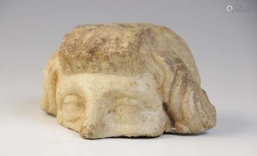 A fragmentary upper half of a head, with carved eyes and wav...