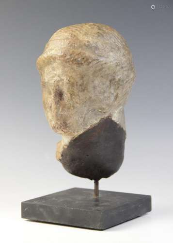 A marble female head, features worn, her hair held in place ...