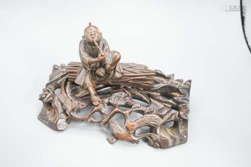 A 19th century Japanese wood okimono of a seated man smoking...