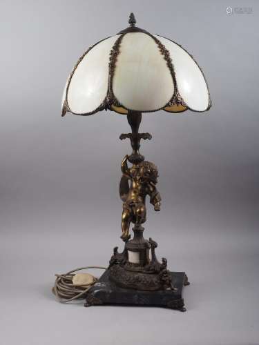 A bronzed table lamp with cherub support and Tiffany style s...