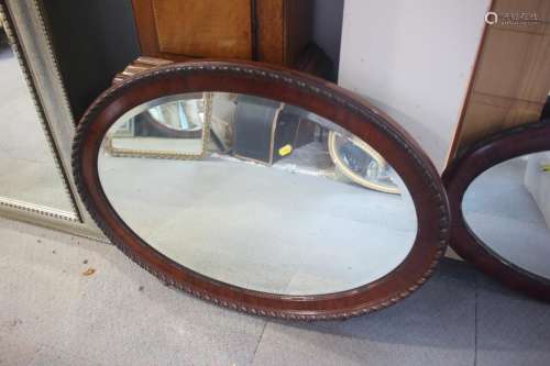 A 1920s mahogany oval framed wall mirror with bevelled plate...