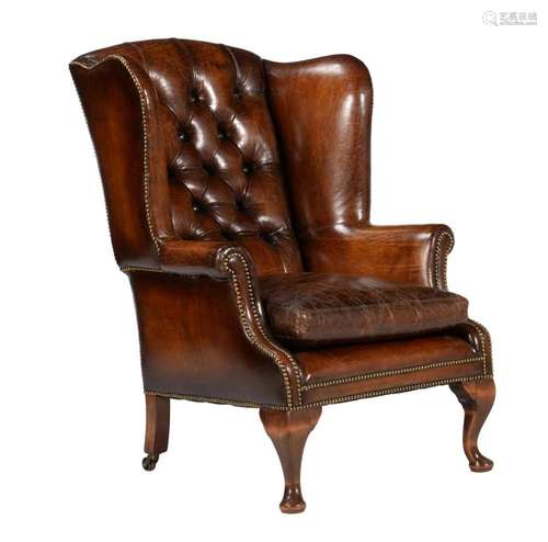 A walnut and leather buttoned wing armchair in George II sty...