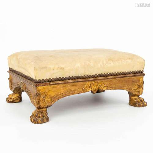 An antique footstool, made of giltwood and standing on claw ...