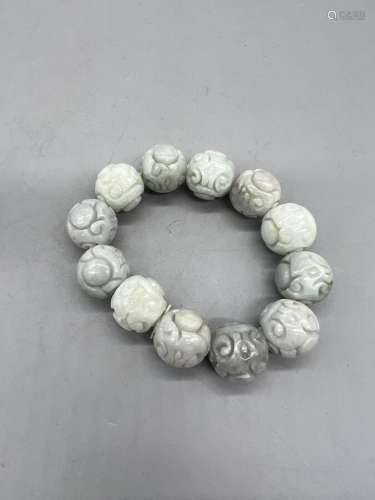 Un bracelet de douze perles de jadéite veinée de vert, sculp...