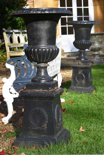 A pair of black painted cast iron campana urns on plinths