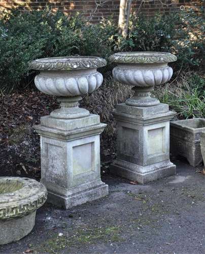 A pair of stone composition garden urns on plinths