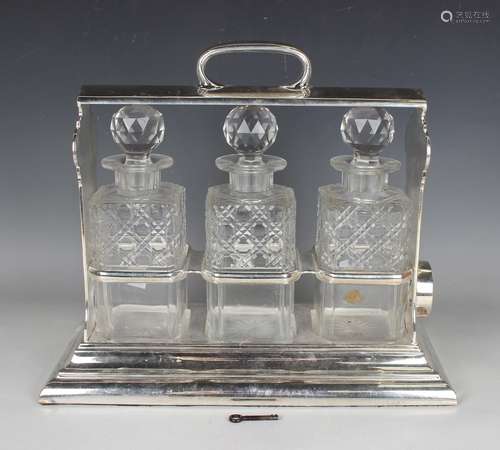 A plated three-bottle tantalus, fitted with three square cut...