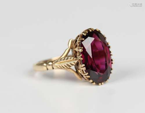 A gold ring, claw set with an oval cut garnet between foliat...