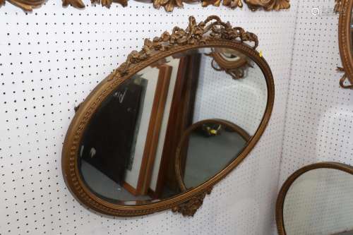 An oval gilt framed wall mirror with ribbon crest plate, 17 ...