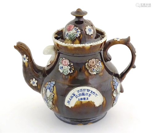 A Victorian treacle glazed bargeware teapot with applied flo...