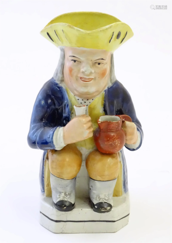 A Toby jug modelled as a seated man holding a beaker and a j...