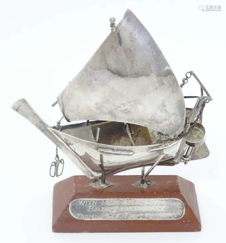 A white metal model of a sailing boat mounted on a wooden st...