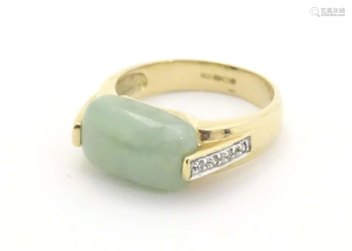 A 9ct gold ring set with pale jade cabochon flanked four dia...
